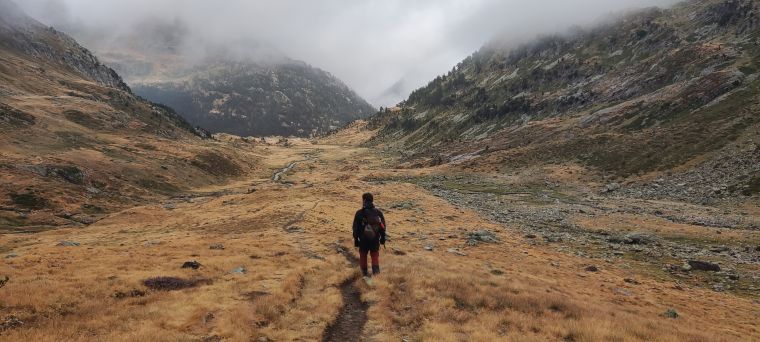 Una figura camina por un valle de montaña bajo la niebla